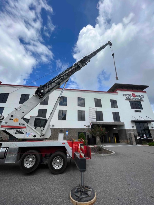Crane lifting a commercial HVAC compressor onto a rooftop for SBS-NC